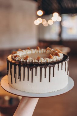 Kafe arka planında çikolata ve karamel olan iştah açıcı büyük beyaz pasta.