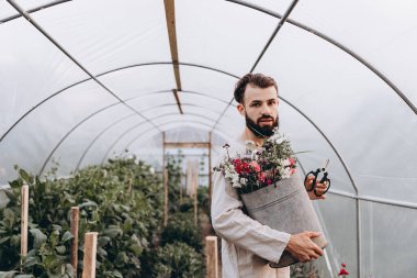 Bahçe yataklarının arasında vazolar ve diğer bitkilerle duran genç ve çekici bahçıvanın fotoğrafı. Metnin için boşluk kopyala