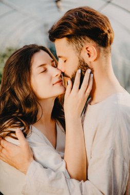 keten giysiler içinde genç otantik bir çift gün batımında çiçek çiftliğindeki kır çiçeklerinin arasında dikilirken, seçici odak noktası, gürültü etkisi