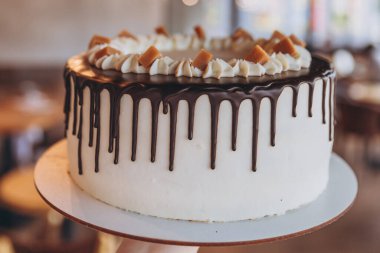 Kafe arka planında çikolata ve karamel olan iştah açıcı büyük beyaz pasta.