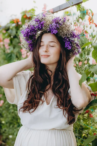 Uzun keten elbise giymiş güzel bir kızın portresi. Çiçeklerin arasında poz veriyor.