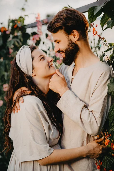 リネンの服を着た愛の男と女の若い本物のカップルは 花の農場 選択的フォーカス ノイズ効果の花のベッドの間に立つ夕日で撮影されています — ストック写真