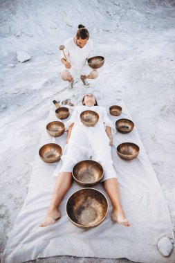 Adam Tibet terapisi yapıyor. Çölde yerde yatan bir kız için. Etrafı bakır kaselerle çevrili.
