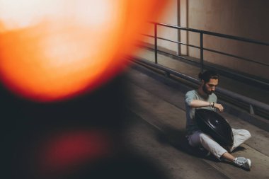 Genç sakallı bir adam yolda otururken pervane çalıyor. Şehir merkezinde müzik ahengi var.