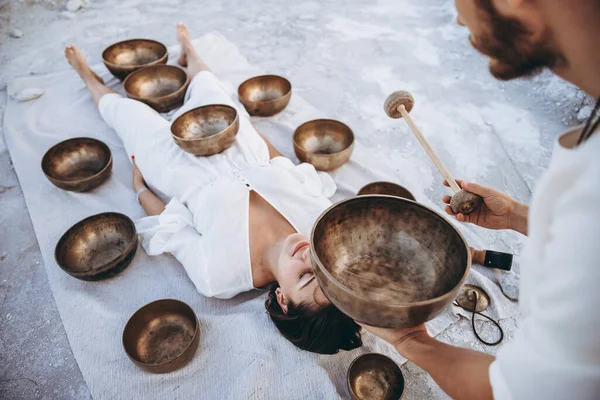 Adam Tibet terapisi yapıyor. Çölde yerde yatan bir kız için. Etrafı bakır kaselerle çevrili.