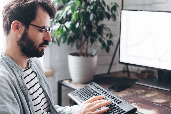 Gözlüklü genç işadamı bilgisayar monitörlerindeki grafikleri kontrol ediyor. Gözlüklü, konsantre olmuş milenyum adamı evde kendini izole etme üzerine çalışıyor.