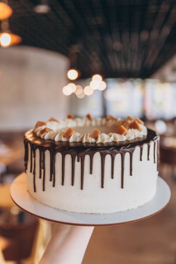 Kafe arka planında çikolata ve karamel olan iştah açıcı büyük beyaz pasta.