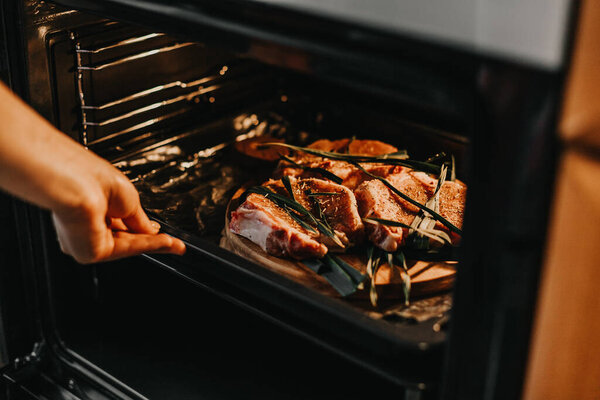 женщина кладет в духовку лист с маринованным мясом для выпечки