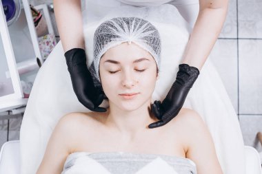 Profesyonel kozmetik uzmanının elleri kaplıca salonunda müşterinin yüzüne maske takar. Kozmetik dolabınızın veya kaplıcanızın reklamını yapmak için ideal bir ortam.