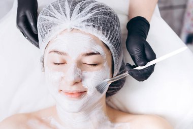 Spa salonu müşterinin yüzüne maske uygulayarak güzellik uzmanı
