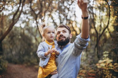 Genç, şık sakallı bir baba gün batımında küçük kızıyla birlikte doğada yürüyor. Baba ve çocuğun aile fotoğrafları. seçici odak, gürültü etkisi