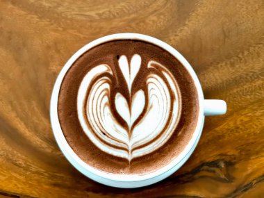 Üstünde latte resmi olan sıcak bir kahve bardağının en üst görüntüsü ahşap masaya konmuş.. 