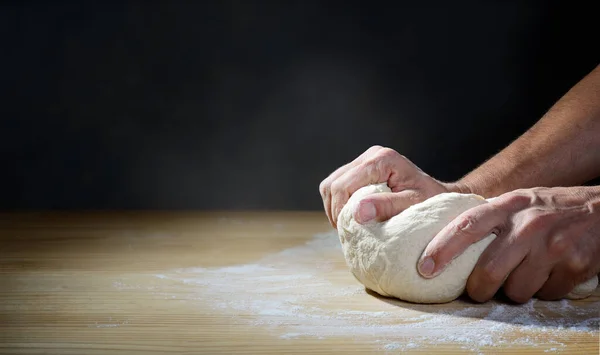 The baker`s hands kneading bread or pizza dough on a wooden pastry board, space for text.