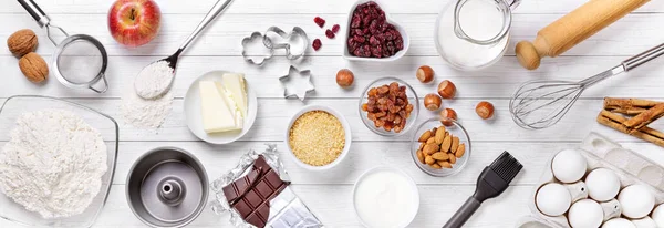 Beyaz ahşap zemin üzerinde kek malzemeleri ve fırın araçları, üst görünüm.
