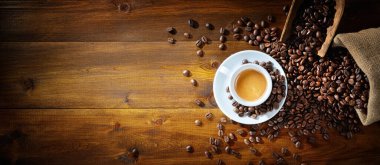 Espresso fincanı ve kahve çekirdekleri ahşap arka planda kepçe ve jüt çuval, üst manzara, metin için boşluk.