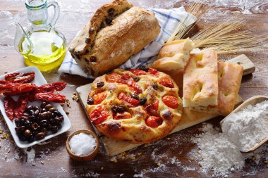 Focaccia Barese ve fırınlanmış ürünler un kaplı bir iş yüzeyinde. Akdeniz diyetinin tipik malzemeleri ve baharatları.