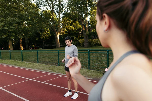 Coach times and gives tips to his young female runner athlete. Selective focus on the man and defocused woman.