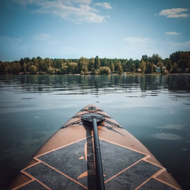 Bir sörf tahtası yeşil ormanın arka planında sakin bir suyu keser