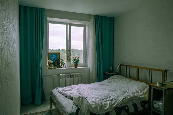 Room with a bed by the window with green curtains