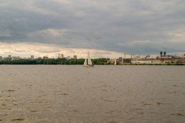 Bir yelkenli gölette yüzüyor, kıyıdan manzaralı.