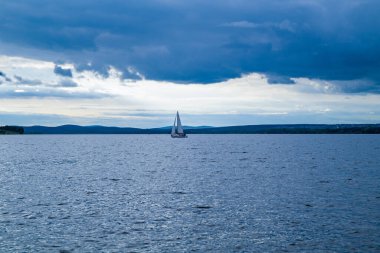 Bir yelkenli gölette yüzüyor, kıyıdan manzaralı.