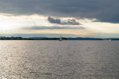 Bir yelkenli gölette yüzüyor, kıyıdan manzaralı.