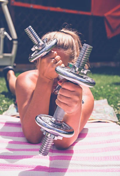 Silver dumbbells in the hands of a girl doing sports in nature