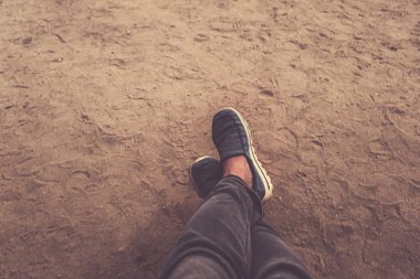 Akşam karanlığında kumun arka planında spor ayakkabılı erkek bacakları.