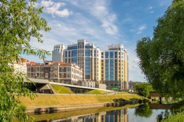 Rıhtımdaki bir ofis binası mavi gökyüzü ve ön plandaki ağaçların arka planına karşı. Şehir manzarası