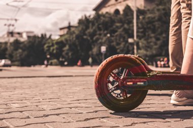 Kaldırım kenarındaki elektrikli scooter 'ın üzerinde duran kadın bacaklarına yaklaş. Yaz günlerinde kot pantolon ve spor ayakkabıları giy.