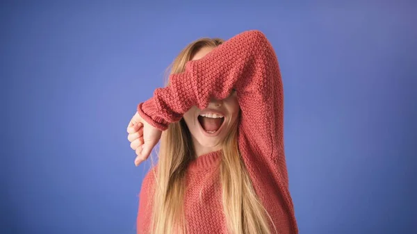 Menina loira bonita rindo em voz alta e cobrindo os olhos com a mão. Isolado em fundo azul — Fotografia de Stock