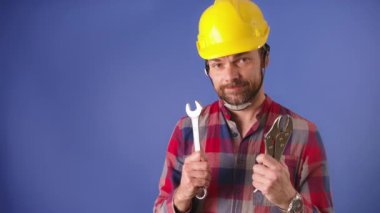 Sakallı, güvenlik kaskı takan ve aletlerini büyük dişli bir gülümsemeyle gösteren yakışıklı bir genç.