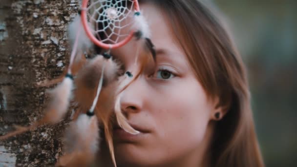 Porträt einer schönen jungen kaukasischen Frau mit grünen Augen, die im Wald in der Nähe von Baumrinde mit Traumfänger in Form ihrer Augen posiert — Stockvideo