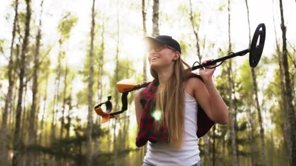 Молодая счастливая белая женщина с металлоискателем на плечах, исследующая лес — стоковое видео