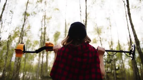 Вид сзади на молодую женщину, поднимающую металлоискатель в воздухе в лесу. Медленное движение — стоковое видео