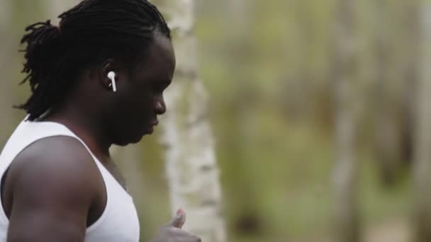 Un africano corriendo por el bosque con auriculares inalámbricos. Lento. — Vídeos de Stock