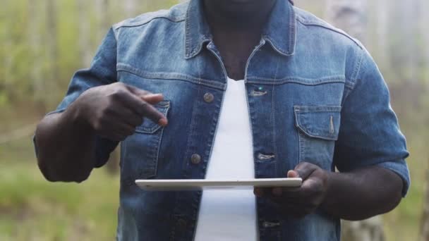 Een Afrikaan die de tablet in het bos gebruikt. draadloos of toekomstig technologieconcept. Sluit geen gezicht. — Stockvideo