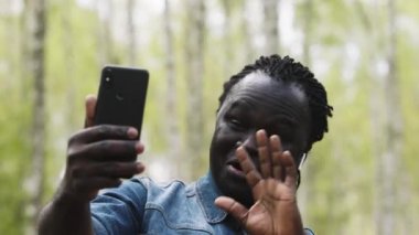 Video görüşmesi için akıllı telefonu kullanan Afrikalı bir adam. Ormandan ailesine el sallıyor.