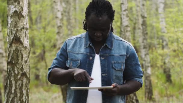 Een Afrikaan die de tablet in het bos gebruikt. draadloos of toekomstig technologieconcept. — Stockvideo