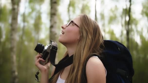 Jovem viajante caucasiano feliz com mochila e câmera vintage cercada por árvores. Retrato tiro em câmera lenta — Vídeo de Stock