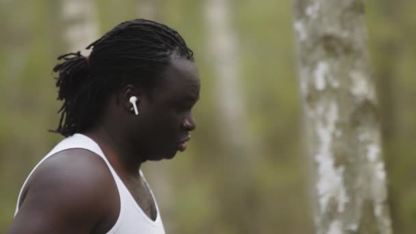 Conceito de perda de peso. Um homem africano a correr na floresta com auscultadores sem fios. Movimento lento — Vídeo de Stock