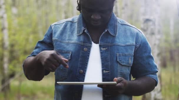 Un hombre africano usando la tableta en el bosque. concepto de tecnología inalámbrica o futura. — Vídeo de stock