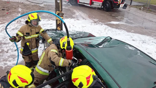 A tűzoltók megpróbálják felvágni a kocsi ajtaját, hogy megmentsék a balesetben érintett személyt. — Stock Fotó