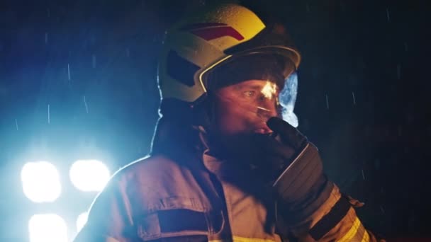 Retrato de un bombero en acción hablando en el walkie talkie. Reflejo de fuego en el casco y reflectores en el fondo. Movimiento lento — Vídeos de Stock