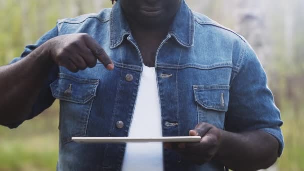 Un hombre africano usando la tableta en el bosque. concepto de tecnología inalámbrica o futura. — Vídeo de stock