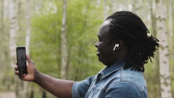 Afrikaanse man neemt selfies of het hebben van videocall op zijn smartphone in de natuur — Stockvideo