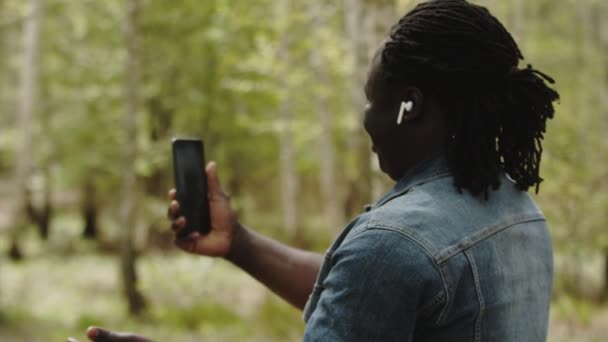 Африканский мужчина делает селфи или имеет видеокамеру на своем смартфоне в природе — стоковое видео