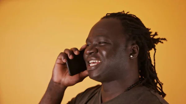 Portrét Afričana, jak vede telefonickou konverzaci. Izolováno na oranžovém pozadí — Stock fotografie