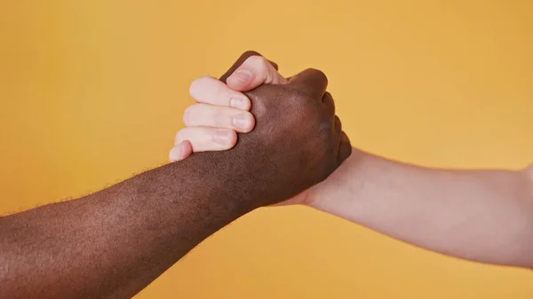 Black and white hands holding together isolated on the orange background. Close up — Stock Photo, Image