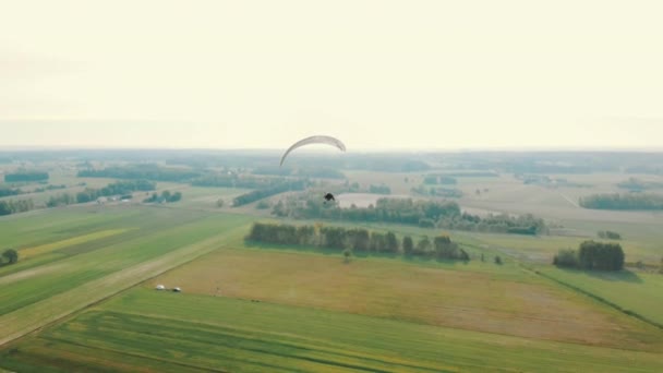 Парамоторный параплан, летящий в воздухе над зелеными полями — стоковое видео